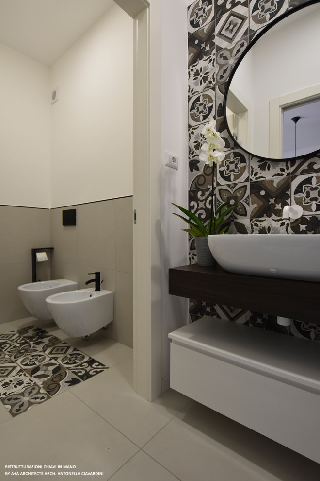 Inredning av ett modernt litet brun brunt toalett, med släta luckor, vita skåp, en toalettstol med separat cisternkåpa, flerfärgad kakel, cementkakel, vita väggar, cementgolv, ett fristående handfat, träbänkskiva och flerfärgat golv