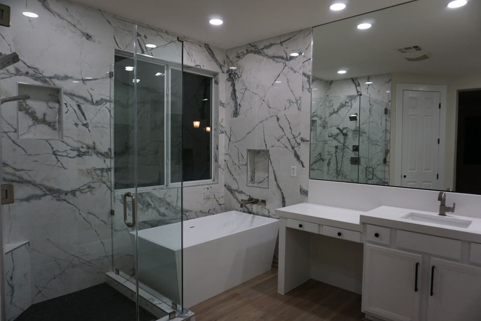 Large modern master bathroom in Las Vegas with raised-panel cabinets, white cabinets, a freestanding tub, a corner shower, a one-piece toilet, white tile, porcelain tile, white walls, vinyl floors, an undermount sink, quartzite benchtops, grey floor, a hinged shower door, white benchtops, an enclosed toilet, a double vanity and a built-in vanity.