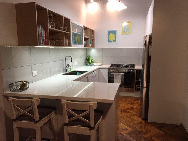 Mid-sized modern u-shaped open plan kitchen in Melbourne with a drop-in sink, flat-panel cabinets, white cabinets, quartz benchtops, grey splashback, porcelain splashback, stainless steel appliances and medium hardwood floors.