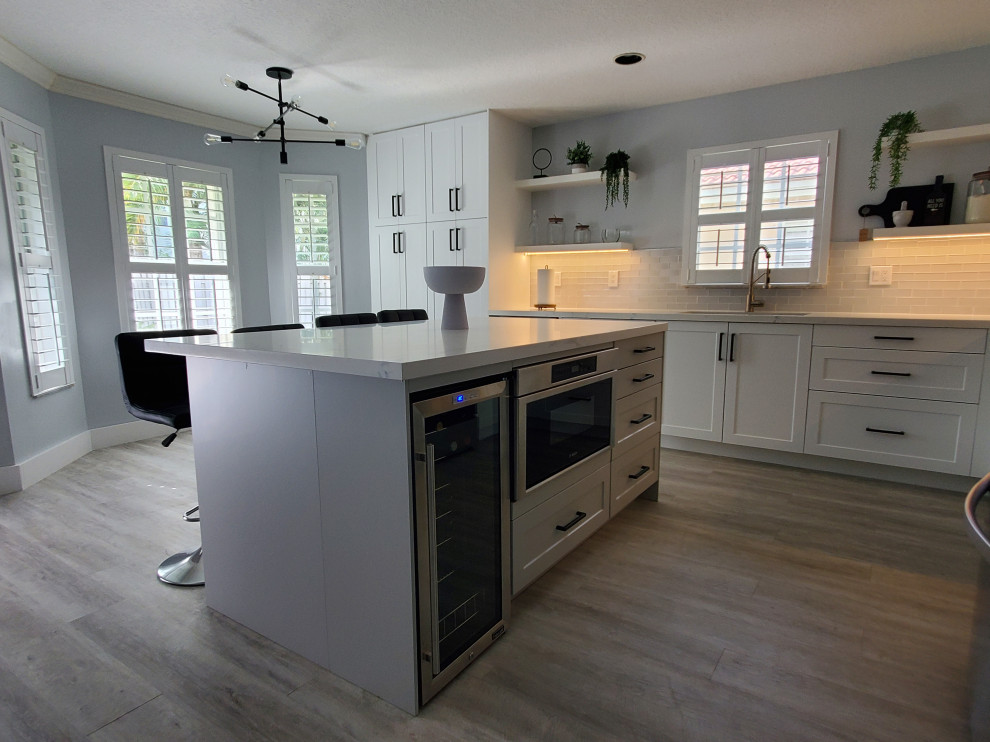 Example of a large transitional l-shaped kitchen pantry design in Miami with shaker cabinets, white cabinets, quartz countertops and an island