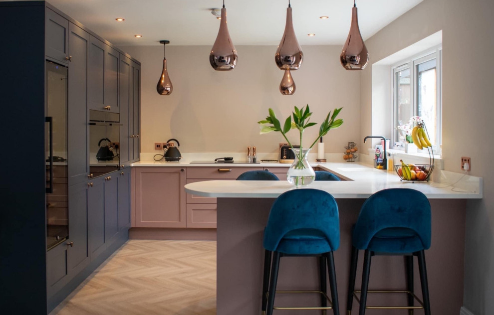 Inspiration for a mid-sized modern u-shaped open plan kitchen in Other with an integrated sink, shaker cabinets, pink cabinets, quartzite benchtops, white splashback, black appliances, a peninsula, brown floor and white benchtop.