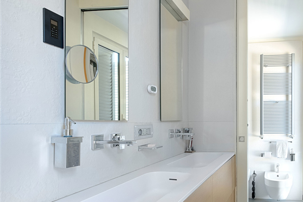 Photo of a mid-sized contemporary 3/4 bathroom in Rome with flat-panel cabinets, light wood cabinets, a curbless shower, a wall-mount toilet, white tile, porcelain tile, white walls, porcelain floors, a drop-in sink, solid surface benchtops, grey floor, a hinged shower door and white benchtops.