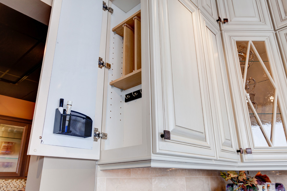 Example of a small classic l-shaped travertine floor and beige floor enclosed kitchen design in Chicago with a farmhouse sink, raised-panel cabinets, white cabinets, granite countertops, beige backsplash, stone tile backsplash, stainless steel appliances and an island