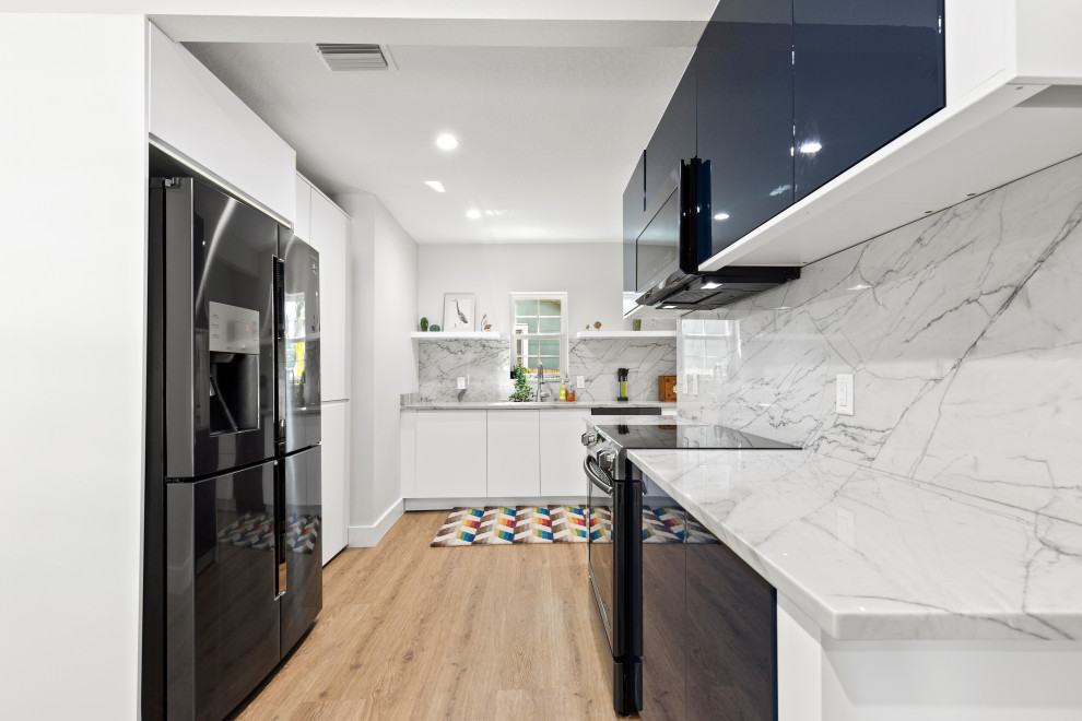 This is an example of a small contemporary l-shaped kitchen in Tampa with an undermount sink, flat-panel cabinets, blue cabinets, granite benchtops, white splashback, granite splashback, vinyl floors, no island, white benchtop, black appliances and brown floor.