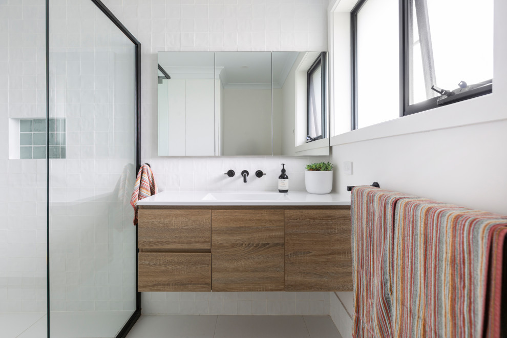 Photo of a medium sized contemporary family bathroom in Canberra - Queanbeyan with freestanding cabinets, medium wood cabinets, a corner shower, a one-piece toilet, white tiles, ceramic tiles, white walls, ceramic flooring, an integrated sink, engineered stone worktops, white floors, a hinged door, white worktops, a single sink and a floating vanity unit.