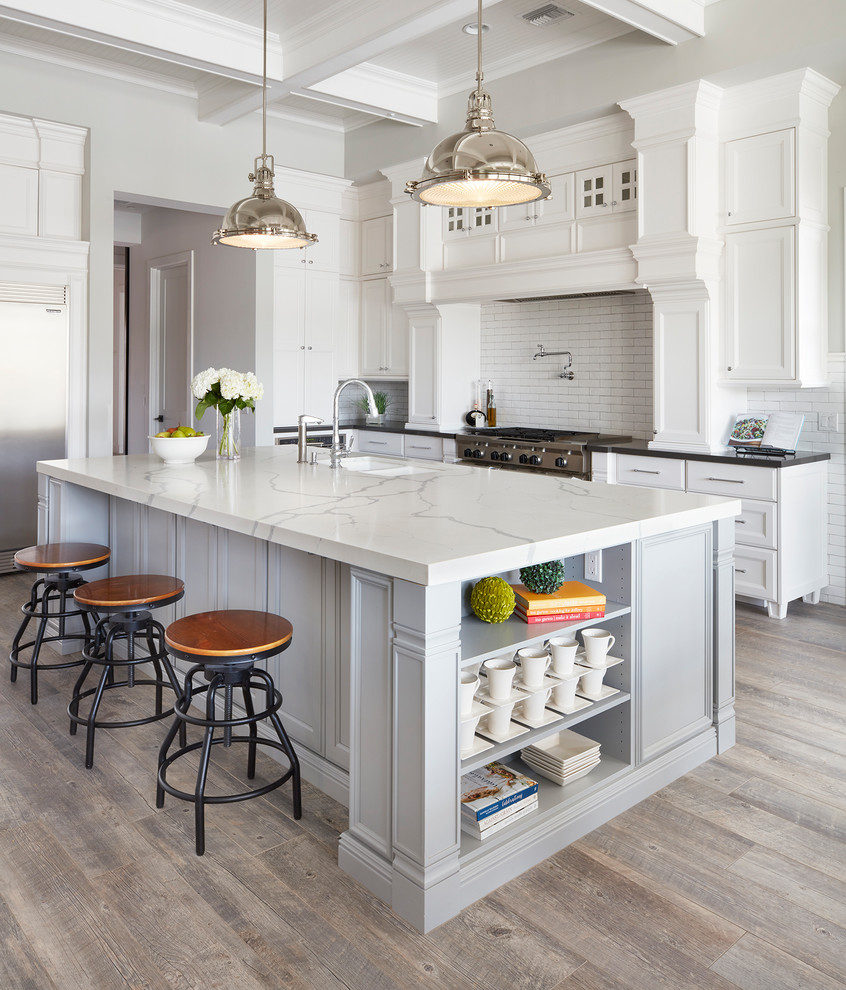 Design ideas for a large traditional l-shaped open plan kitchen in Phoenix with an undermount sink, recessed-panel cabinets, white cabinets, quartz benchtops, white splashback, ceramic splashback, stainless steel appliances, ceramic floors, with island and brown floor.