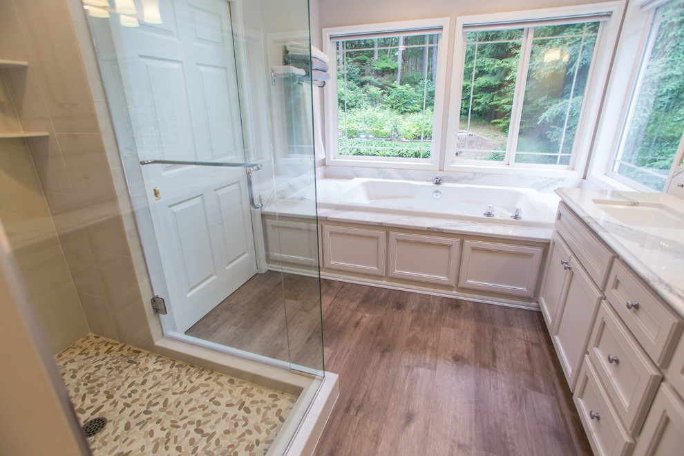 Mid-sized traditional master bathroom in Seattle with beaded inset cabinets, beige cabinets, a corner tub, a corner shower, white tile, stone slab, grey walls, light hardwood floors, an undermount sink, quartzite benchtops, grey floor, a hinged shower door and white benchtops.