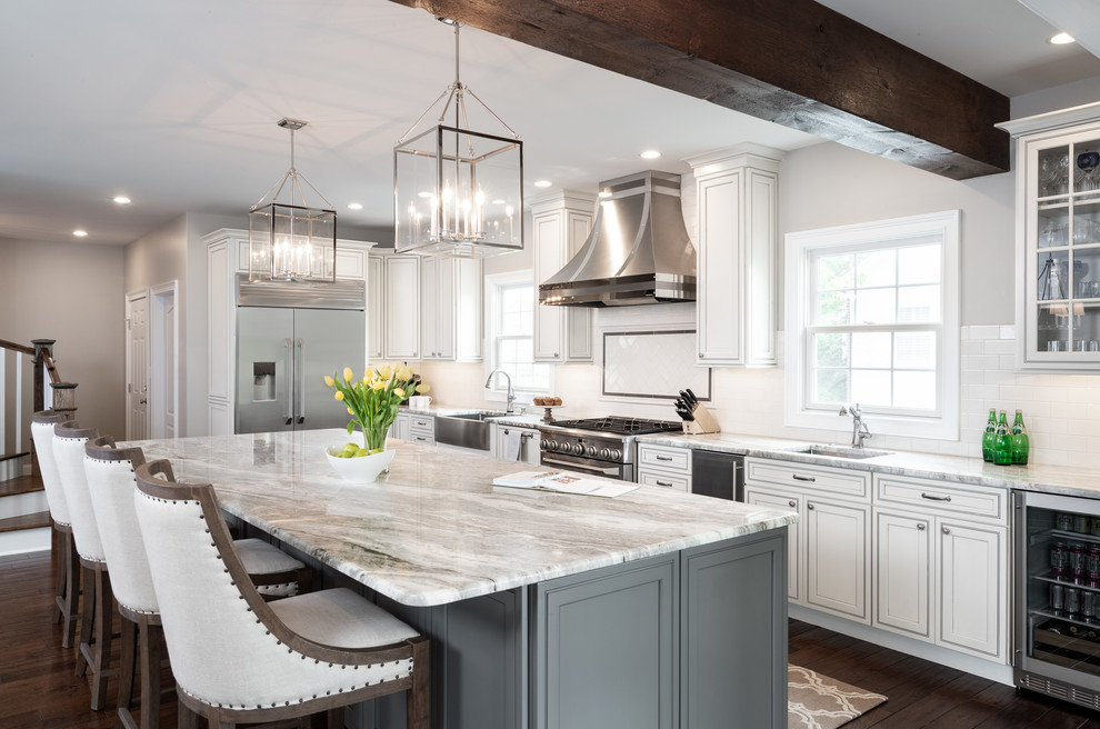 Design ideas for a country l-shaped kitchen in Philadelphia with a farmhouse sink, recessed-panel cabinets, white cabinets, white splashback, stainless steel appliances, dark hardwood floors, with island, brown floor and beige benchtop.