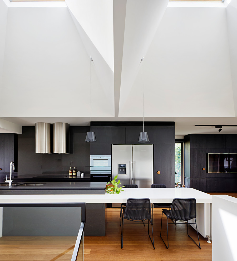 Photo of a mid-sized contemporary galley open plan kitchen in Melbourne with a double-bowl sink, dark wood cabinets, quartz benchtops, black splashback, stainless steel appliances, medium hardwood floors, with island and brown floor.