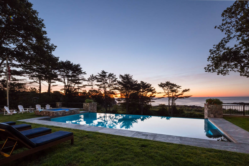 Large traditional backyard rectangular infinity pool in Portland Maine with a pool house and concrete slab.