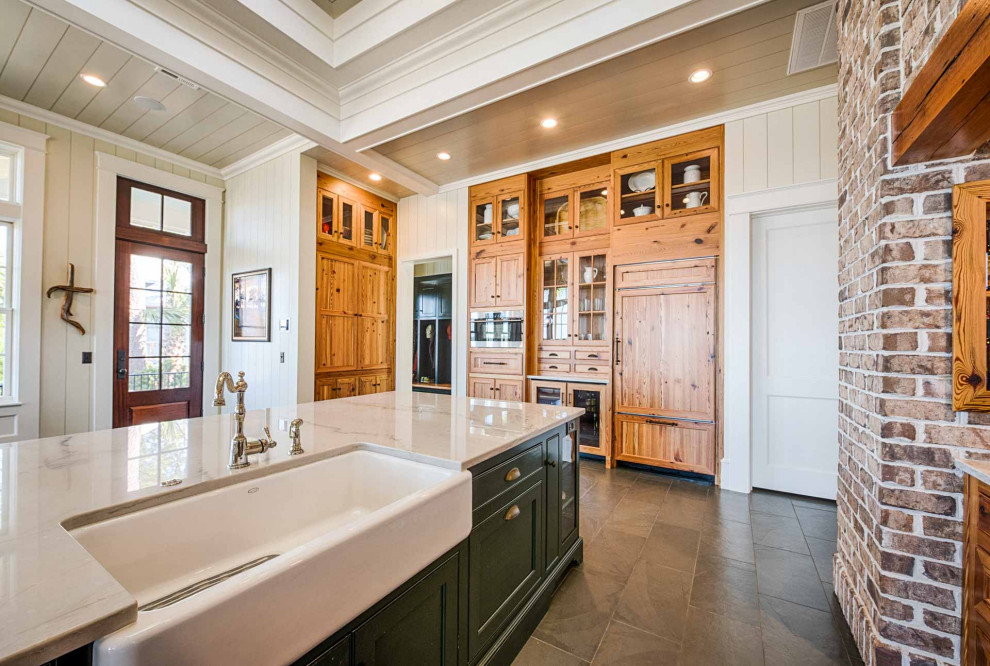 Bild på ett vit vitt kök, med en rustik diskho, luckor med infälld panel, skåp i mellenmörkt trä, marmorbänkskiva, grått stänkskydd, stänkskydd i keramik, skiffergolv, en köksö och grått golv
