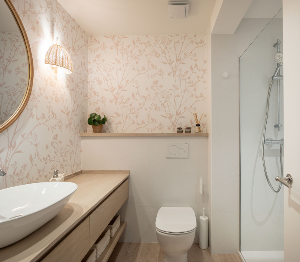 Стильный дизайн: ванная комната среднего размера в стиле неоклассика (современная классика) с плоскими фасадами, белыми фасадами, душем без бортиков, инсталляцией, розовой плиткой, белыми стенами, полом из ламината, душевой кабиной, настольной раковиной, столешницей из ламината, коричневым полом, душем с раздвижными дверями, коричневой столешницей, тумбой под одну раковину, встроенной тумбой и обоями на стенах - последний тренд