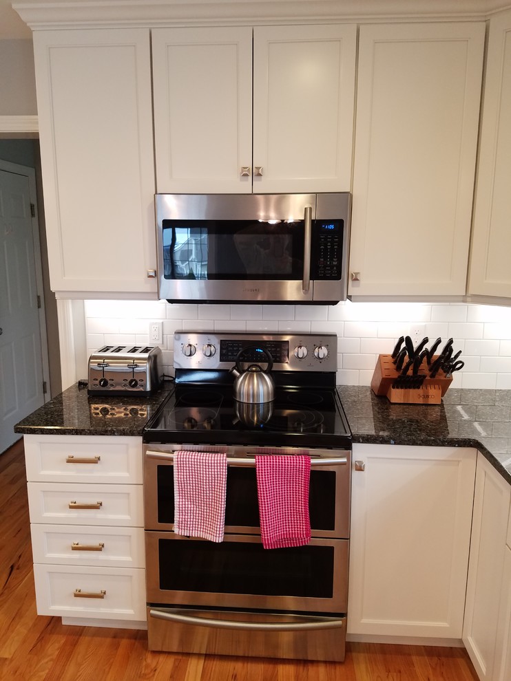 Large transitional l-shaped light wood floor and brown floor eat-in kitchen photo with an undermount sink, shaker cabinets, white cabinets, granite countertops, white backsplash, subway tile backsplash, stainless steel appliances and an island