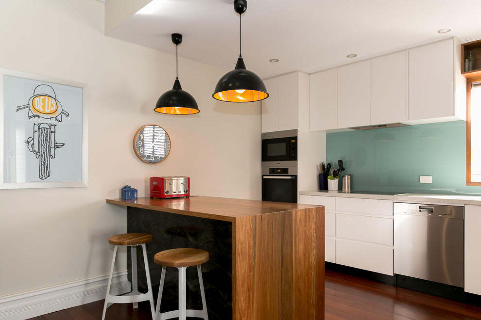 This is an example of a mid-sized contemporary galley eat-in kitchen in Perth with flat-panel cabinets, white cabinets, blue splashback, glass sheet splashback, a peninsula, an undermount sink, quartz benchtops, stainless steel appliances and medium hardwood floors.