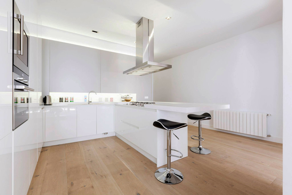 Photo of a mid-sized contemporary u-shaped separate kitchen in Madrid with flat-panel cabinets, white cabinets, light hardwood floors, a peninsula, solid surface benchtops, white splashback and white benchtop.