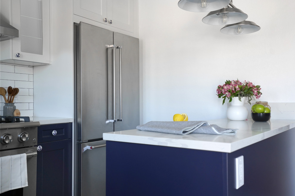 Bild på ett mellanstort maritimt vit vitt kök, med en rustik diskho, skåp i shakerstil, blå skåp, bänkskiva i kvarts, vitt stänkskydd, stänkskydd i tunnelbanekakel, rostfria vitvaror, klinkergolv i keramik, en köksö och flerfärgat golv