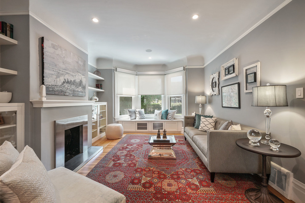 Photo of a transitional living room in San Francisco with grey walls, medium hardwood floors, a standard fireplace, a metal fireplace surround and brown floor.