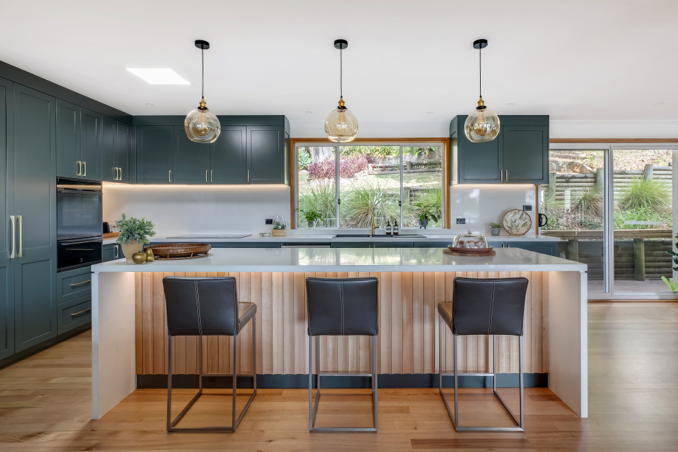 Inspiration for a large transitional l-shaped medium tone wood floor and multicolored floor eat-in kitchen remodel in Sydney with a drop-in sink, shaker cabinets, green cabinets, quartz countertops, white backsplash, quartz backsplash, black appliances, an island and white countertops