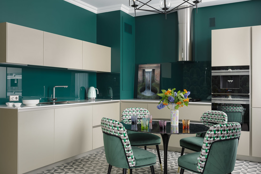 Photo of a contemporary l-shaped eat-in kitchen in Saint Petersburg with a drop-in sink, flat-panel cabinets, beige cabinets, green splashback, glass sheet splashback, black appliances, no island, multi-coloured floor and white benchtop.