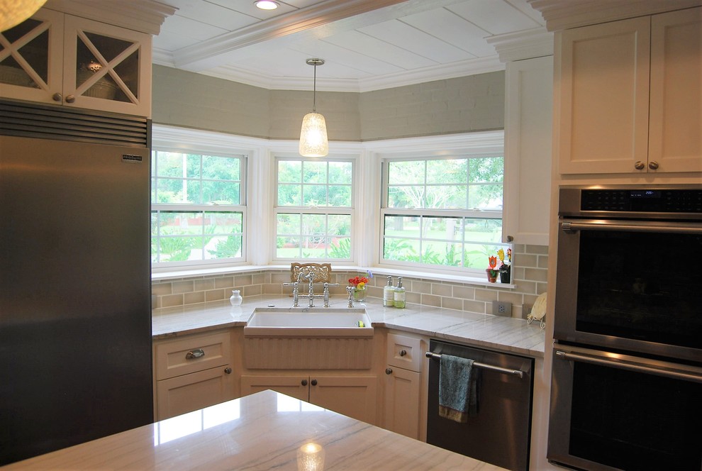 Inspiration for a mid-sized transitional u-shaped light wood floor kitchen remodel in Austin with a farmhouse sink, shaker cabinets, white cabinets, quartzite countertops, beige backsplash, porcelain backsplash, stainless steel appliances and an island