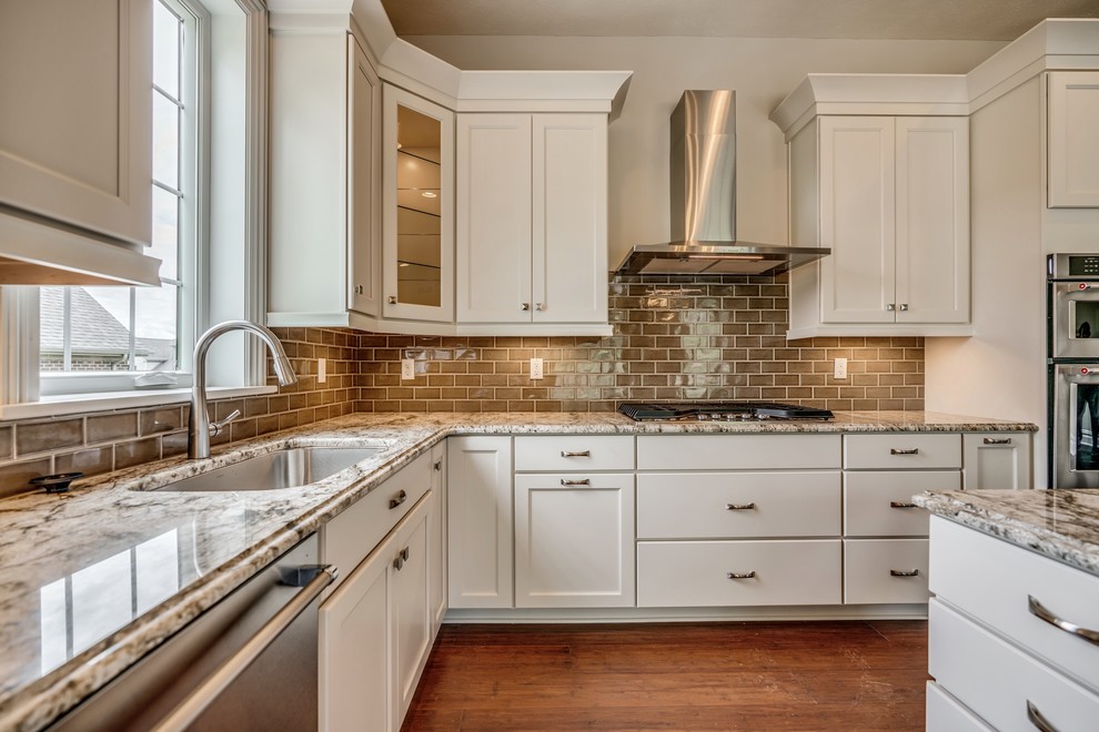 Example of a transitional l-shaped bamboo floor and brown floor eat-in kitchen design with an undermount sink, flat-panel cabinets, white cabinets, granite countertops, brown backsplash, subway tile backsplash, stainless steel appliances, an island and brown countertops