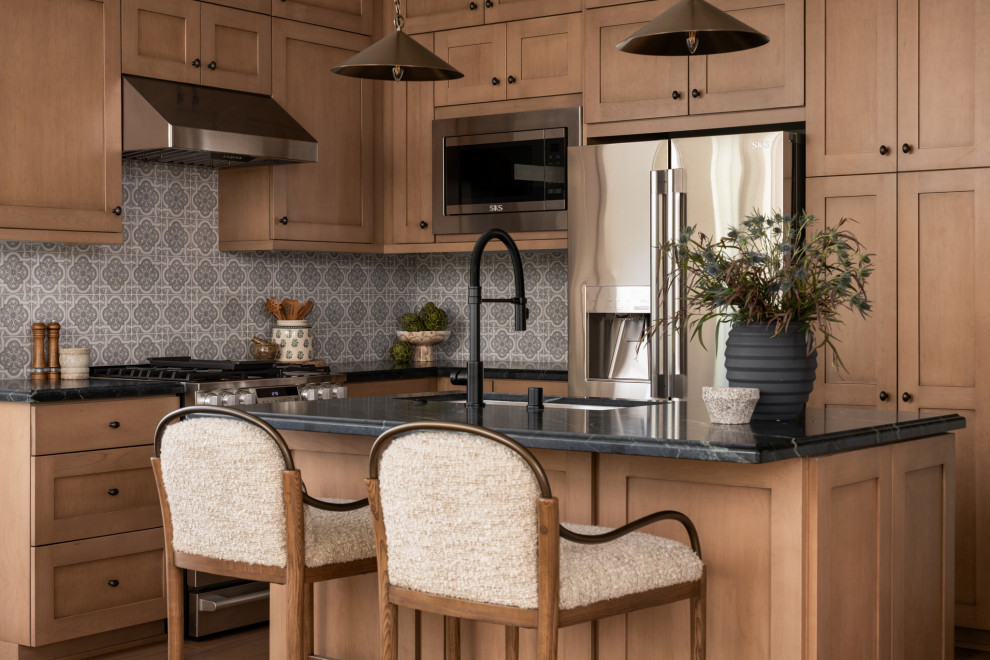 Eat-in kitchen - mediterranean l-shaped medium tone wood floor and brown floor eat-in kitchen idea in Los Angeles with an undermount sink, shaker cabinets, brown cabinets, multicolored backsplash, ceramic backsplash, stainless steel appliances, an island and black countertops