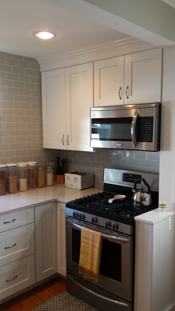Enclosed kitchen - small transitional u-shaped light wood floor enclosed kitchen idea in New York with an undermount sink, shaker cabinets, white cabinets, solid surface countertops, gray backsplash, subway tile backsplash, stainless steel appliances and an island