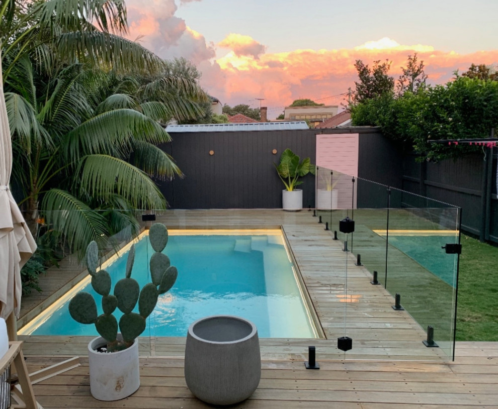 Diseño de piscina tropical de tamaño medio rectangular en patio trasero con paisajismo de piscina y entablado