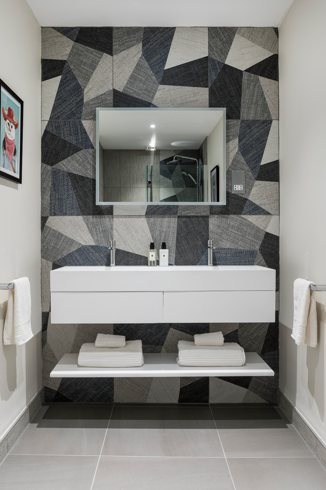 This is an example of a mid-sized transitional master bathroom in Cheshire with flat-panel cabinets, white cabinets, blue tile, white walls, ceramic floors, a wall-mount sink, solid surface benchtops and grey floor.