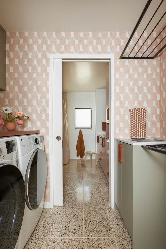 Small retro galley separated utility room in San Francisco with a submerged sink, flat-panel cabinets, green cabinets, engineered stone countertops, pink walls, concrete flooring, a side by side washer and dryer, brown floors, grey worktops and wallpapered walls.