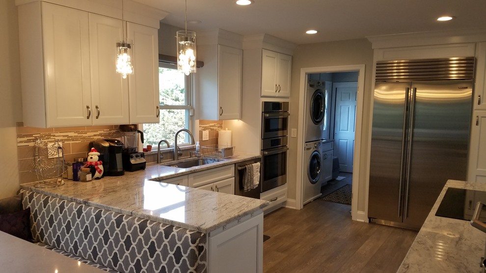 Mid-sized transitional u-shaped medium tone wood floor and brown floor eat-in kitchen photo in Philadelphia with an undermount sink, recessed-panel cabinets, white cabinets, granite countertops, gray backsplash, glass tile backsplash, stainless steel appliances and a peninsula