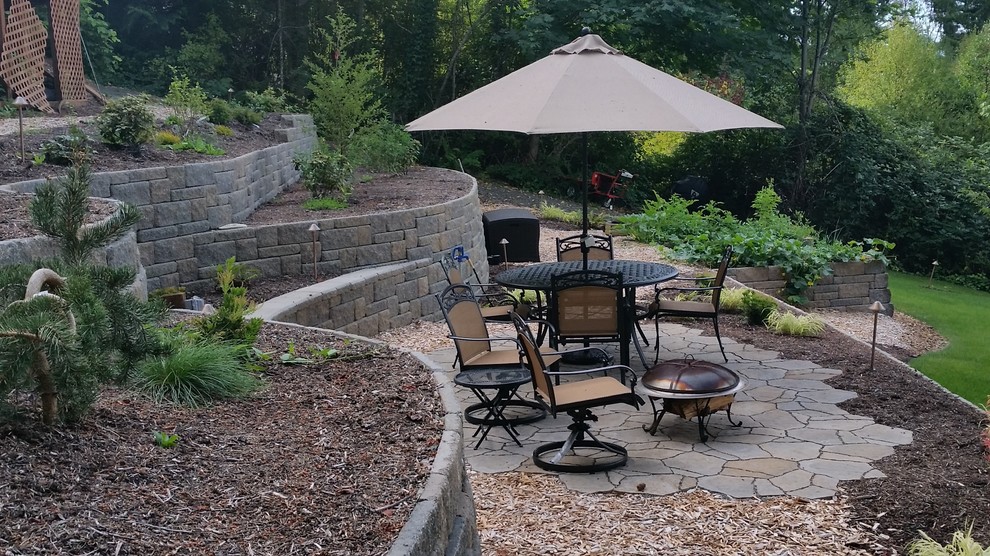 Large traditional sloped partial sun garden in Seattle with a retaining wall and natural stone pavers.