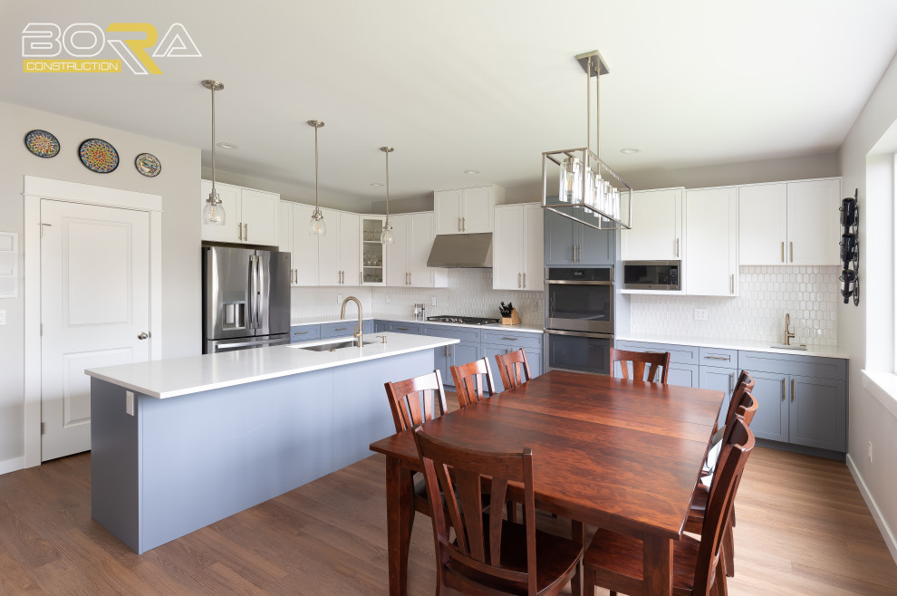 Inspiration for a large transitional l-shaped medium tone wood floor and brown floor eat-in kitchen remodel in Seattle with an undermount sink, shaker cabinets, blue cabinets, quartz countertops, white backsplash, ceramic backsplash, stainless steel appliances, an island and white countertops