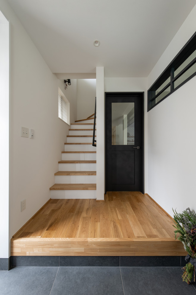 Mid-sized urban medium tone wood floor, wallpaper ceiling and wallpaper entryway photo in Other with white walls and a medium wood front door