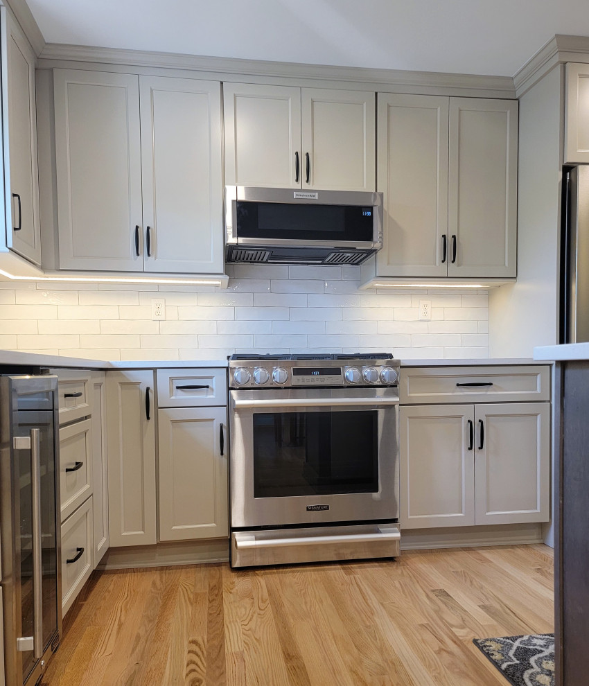 Mid-sized transitional l-shaped medium tone wood floor and yellow floor eat-in kitchen photo with an undermount sink, flat-panel cabinets, gray cabinets, quartz countertops, white backsplash, ceramic backsplash, stainless steel appliances, an island and white countertops