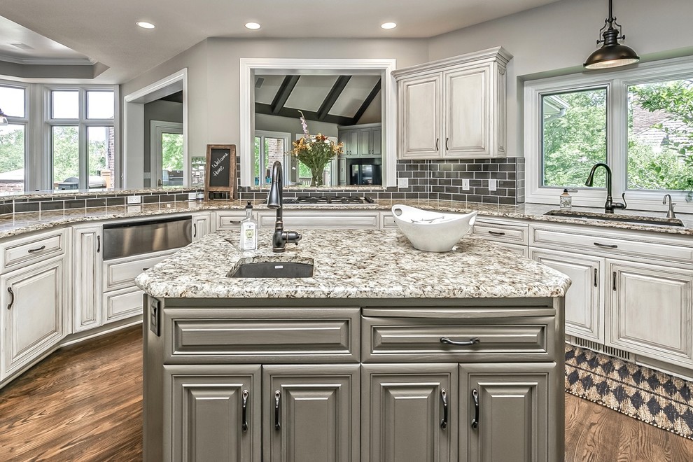 This is an example of a large beach style u-shaped eat-in kitchen in Omaha with an undermount sink, recessed-panel cabinets, white cabinets, granite benchtops, grey splashback, glass tile splashback, stainless steel appliances, dark hardwood floors and with island.