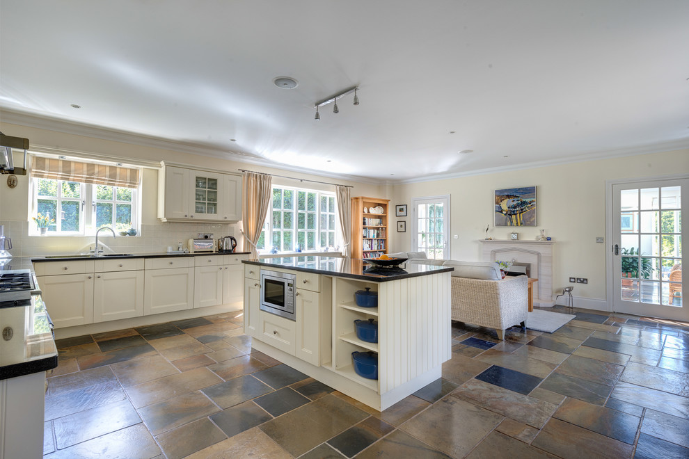 Photo of a mid-sized country open plan kitchen in Devon with recessed-panel cabinets, white cabinets, white splashback, ceramic splashback, stainless steel appliances and multi-coloured floor.