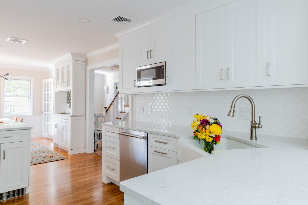 Design ideas for a large transitional u-shaped kitchen pantry in Boston with a farmhouse sink, recessed-panel cabinets, white cabinets, quartz benchtops, white splashback, ceramic splashback, stainless steel appliances, medium hardwood floors, no island, brown floor and white benchtop.