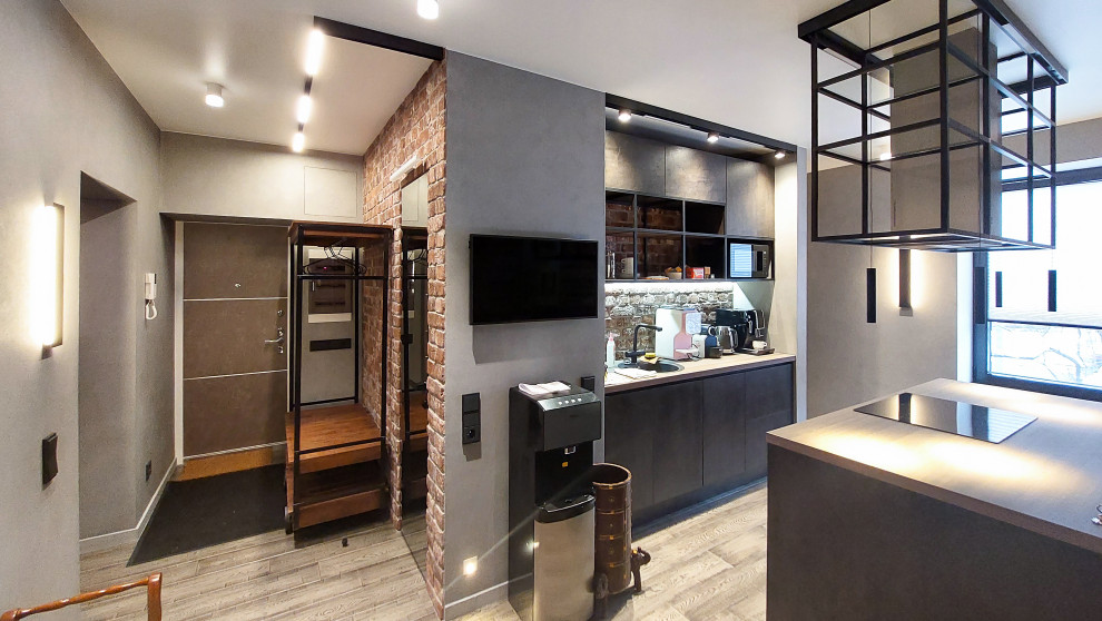 Photo of a large industrial galley eat-in kitchen in Moscow with an undermount sink, flat-panel cabinets, black cabinets, wood benchtops, brown splashback, brick splashback, stainless steel appliances, medium hardwood floors, with island, brown floor and brown benchtop.