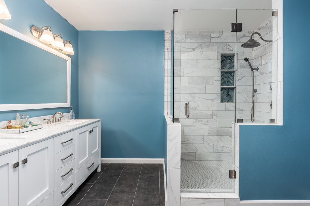 This is an example of a small transitional master bathroom in Dallas with shaker cabinets, white cabinets, a corner shower, a one-piece toilet, white tile, porcelain tile, blue walls, porcelain floors, an undermount sink, marble benchtops, grey floor and a hinged shower door.