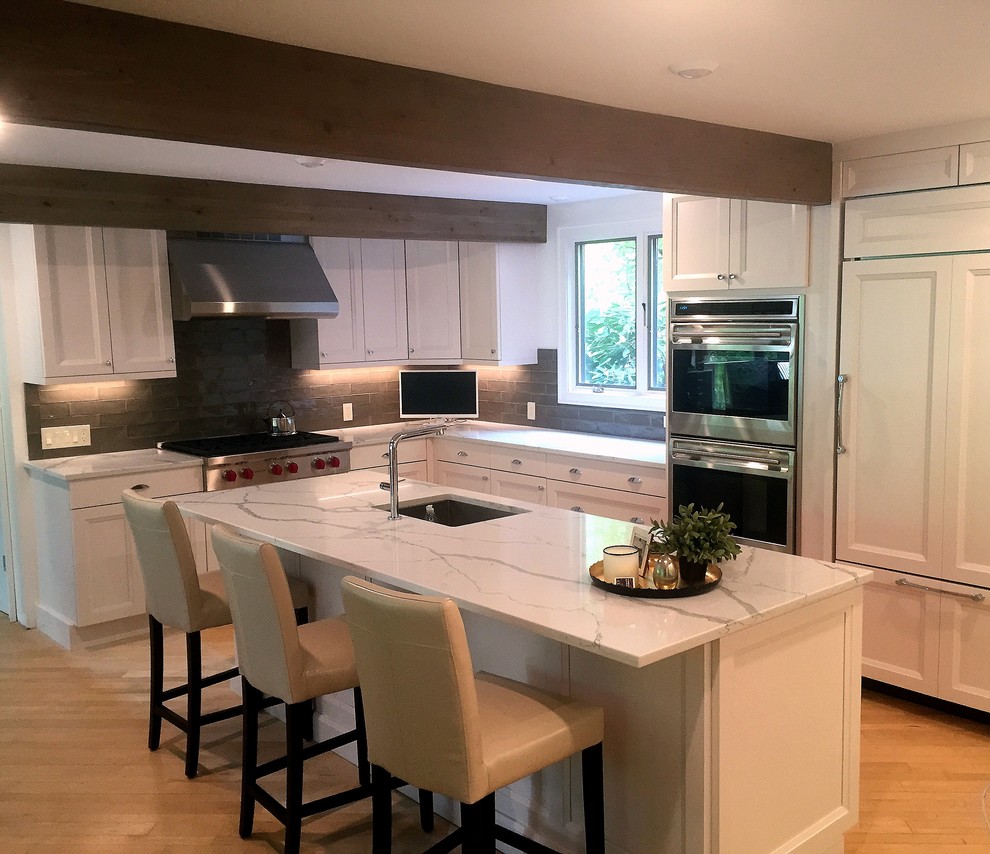 Inspiration for a mid-sized transitional l-shaped light wood floor and brown floor enclosed kitchen remodel in Boston with an undermount sink, recessed-panel cabinets, white cabinets, quartzite countertops, gray backsplash, glass tile backsplash, an island, paneled appliances and white countertops