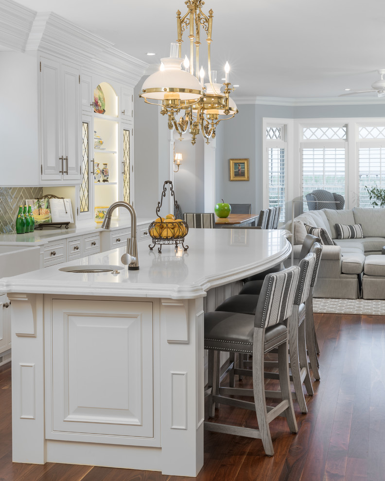 Expansive traditional u-shaped eat-in kitchen in Newark with with island, raised-panel cabinets, white cabinets, quartz benchtops, grey splashback, ceramic splashback, white benchtop, medium hardwood floors, a farmhouse sink, panelled appliances and brown floor.