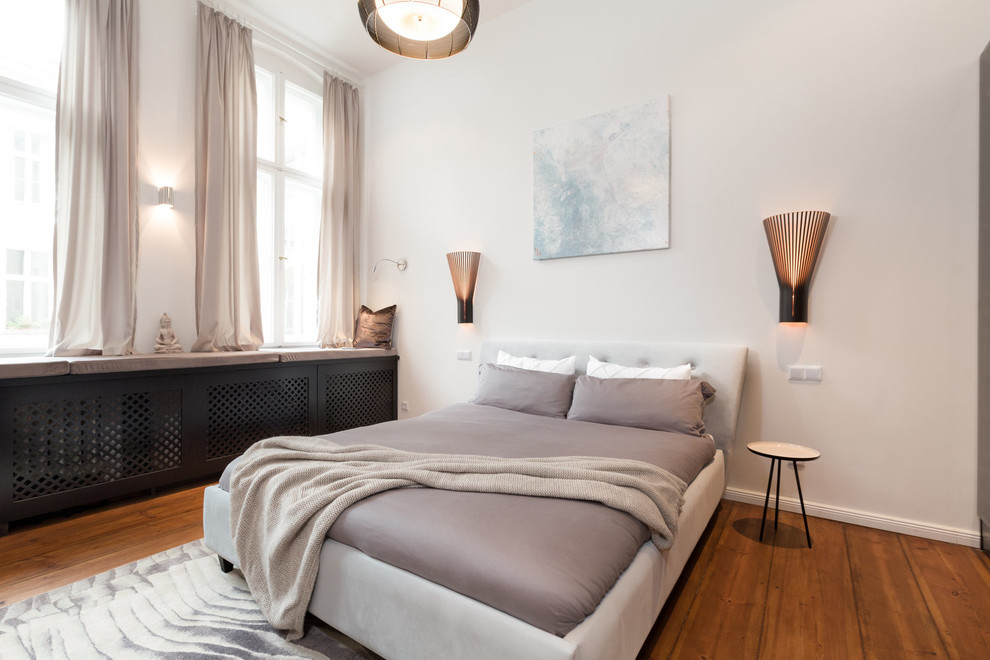 This is an example of a mid-sized contemporary master bedroom in Berlin with white walls, medium hardwood floors and brown floor.