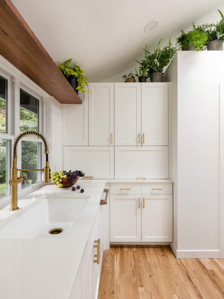 Foto på ett mellanstort minimalistiskt vit kök, med en undermonterad diskho, luckor med infälld panel, vita skåp, bänkskiva i kvarts, vitt stänkskydd, stänkskydd i tunnelbanekakel, vita vitvaror, ljust trägolv och en köksö