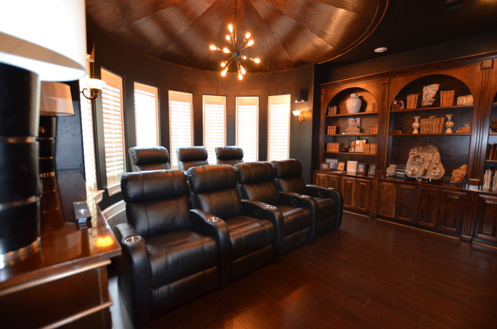 This is an example of an enclosed home theatre in Austin with black walls, dark hardwood floors and a wall-mounted tv.
