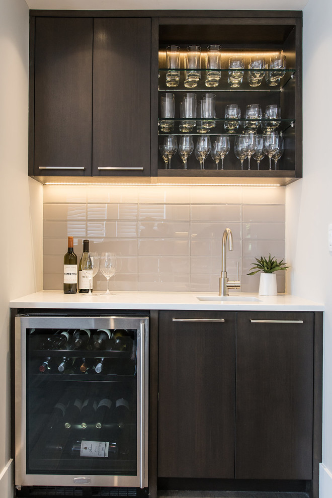 Photo of a small modern single-wall wet bar in Vancouver with an undermount sink, flat-panel cabinets, dark wood cabinets, solid surface benchtops, beige splashback, glass tile splashback, dark hardwood floors, brown floor and white benchtop.