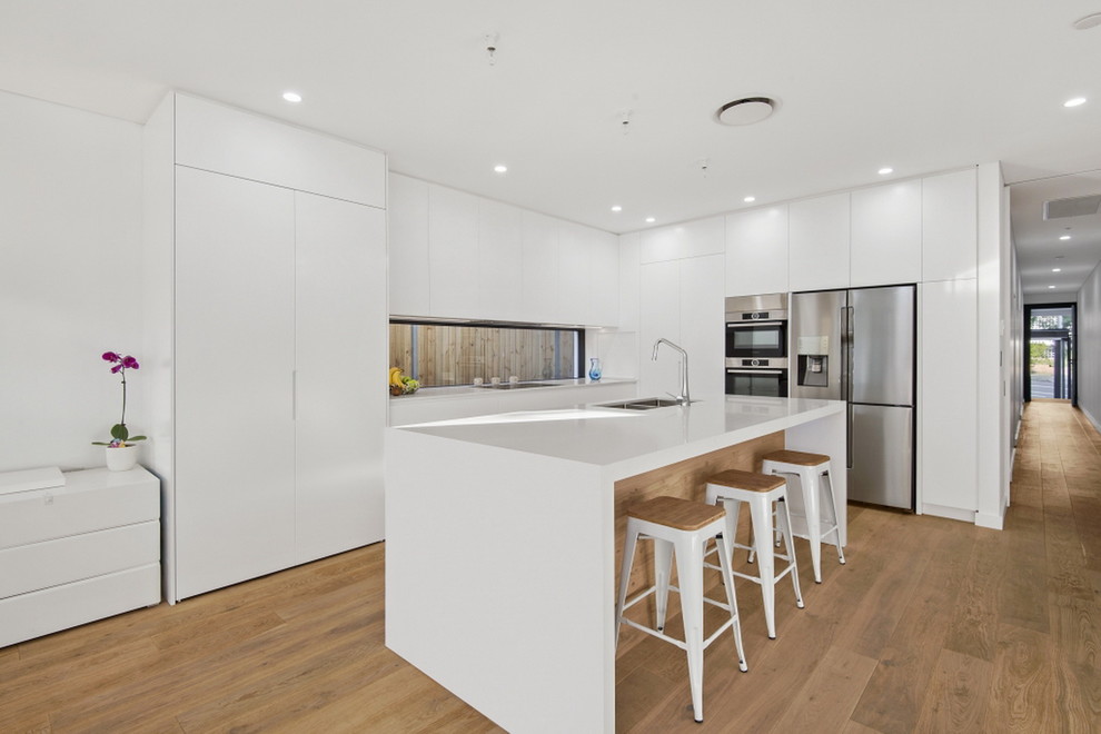 Inspiration for a mid-sized modern galley eat-in kitchen in Sydney with a drop-in sink, recessed-panel cabinets, white cabinets, quartz benchtops, light hardwood floors, with island, brown floor and white benchtop.