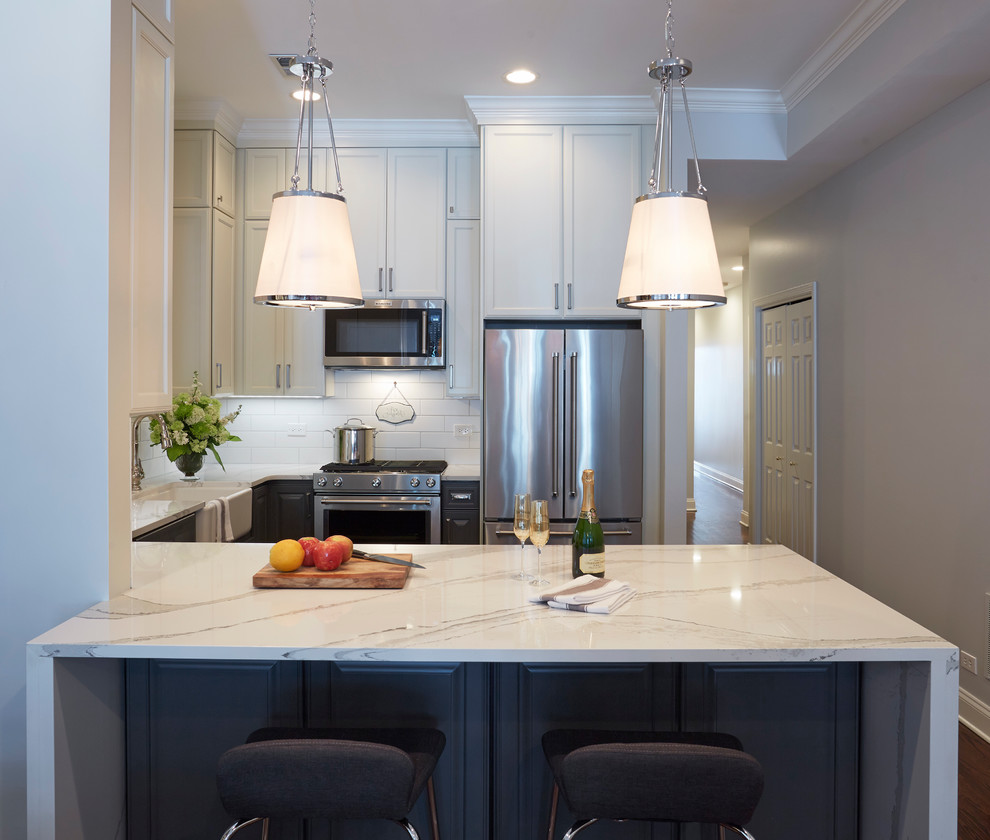 This is an example of a mid-sized transitional u-shaped eat-in kitchen in Chicago with a farmhouse sink, shaker cabinets, white cabinets, marble benchtops, white splashback, subway tile splashback, stainless steel appliances, dark hardwood floors and a peninsula.