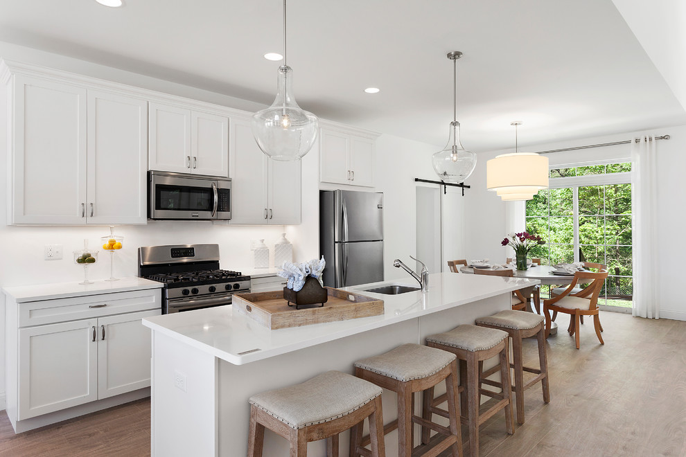 Beach style eat-in kitchen in New York with an undermount sink, shaker cabinets, white cabinets, white splashback, stainless steel appliances, light hardwood floors, with island and beige floor.