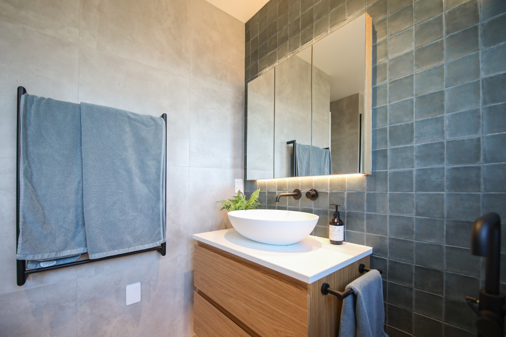 Inspiration for a mid-sized modern bathroom in Christchurch with furniture-like cabinets, light wood cabinets, a freestanding tub, gray tile, ceramic tile, grey walls, ceramic floors, a console sink, granite benchtops, grey floor, white benchtops, a single vanity and a floating vanity.